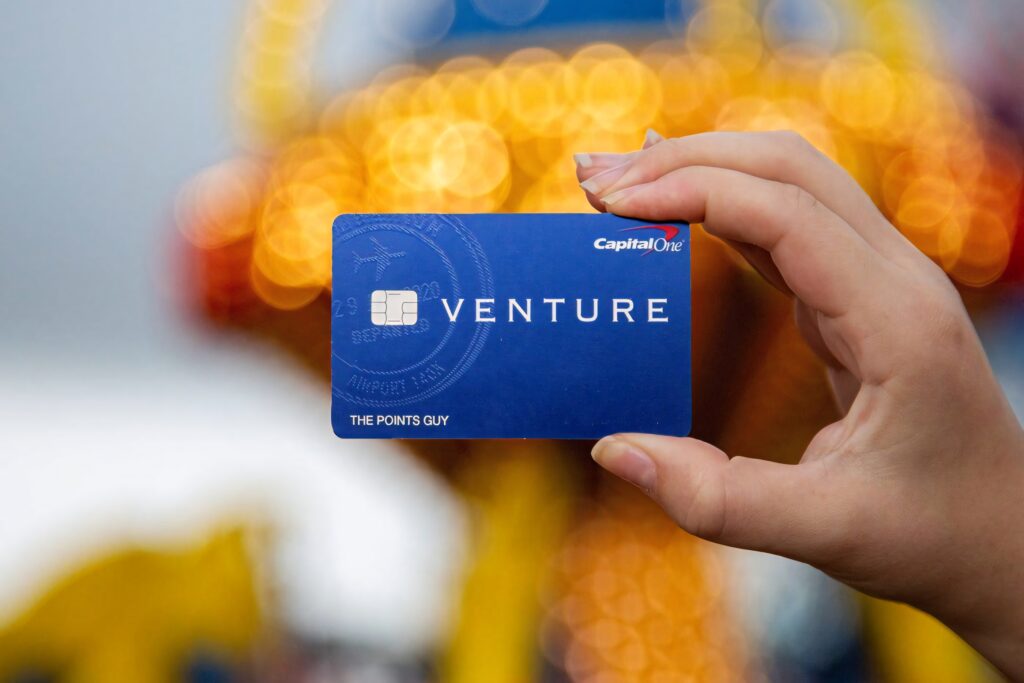 Hand holding blue Capital One Venture credit card with blurred warm yellow light background Wallpaper