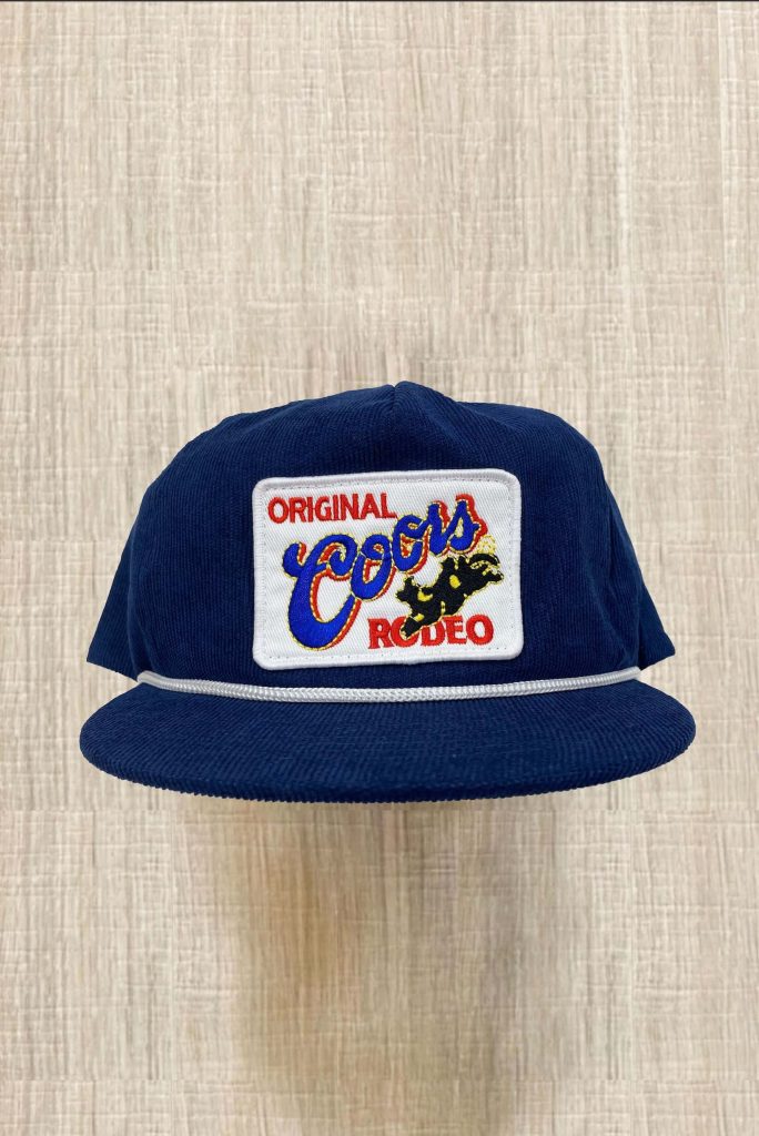 Blue corduroy trucker cap with Original Coors Rodeo patch on light wood grain background Wallpaper