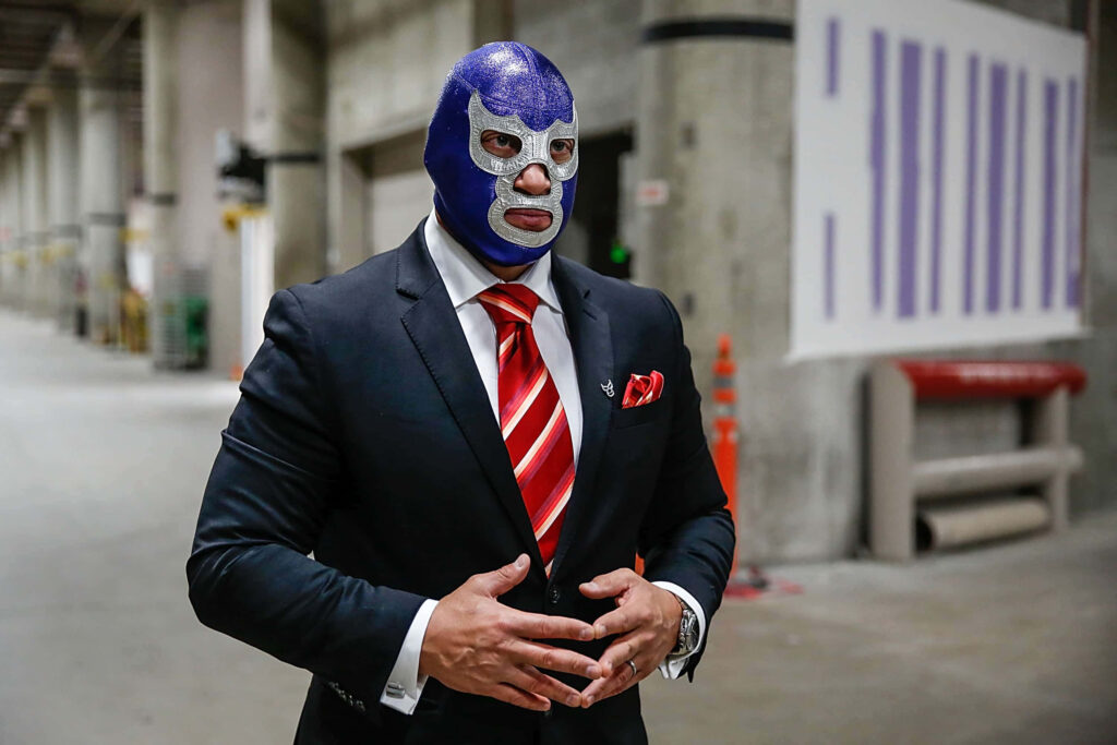 Man in sharp suit and red tie wearing blue Blue Demon lucha libre mask industrial background Wallpaper