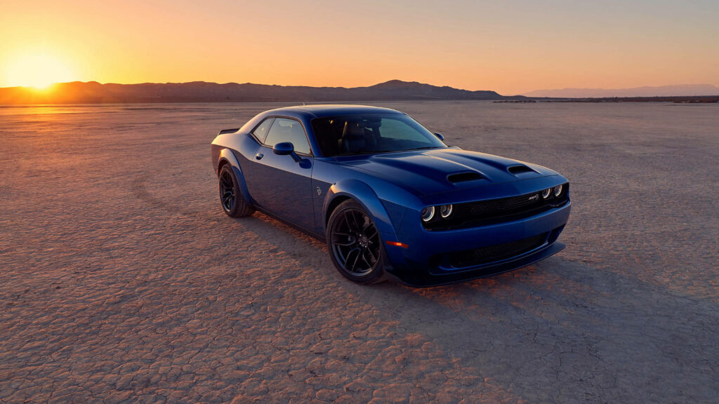 Blue Dodge Challenger parked on desert flat at sunset with golden glow and distant mountains background Wallpaper