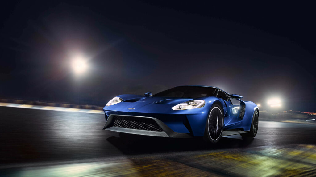 Blue Ford GT luxury car racing at night on illuminated racetrack with sleek aerodynamic design Wallpaper