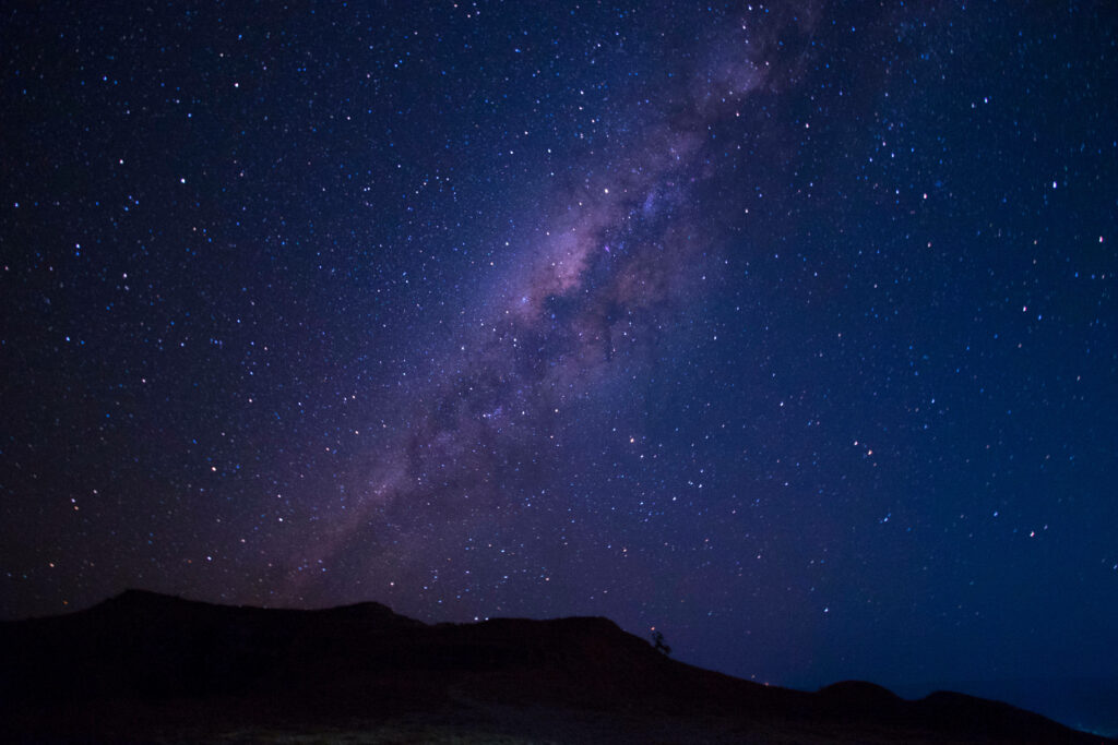Blue Galaxy Splendor: Majestic Mountain Silhouette Underneath a Twinkling Blue, Purple, and Pink Starry Night Sky Wallpaper