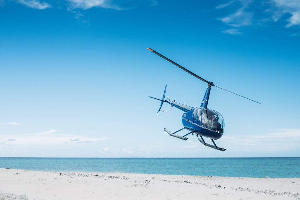 Blue helicopter flying over white sand beach with clear sky and turquoise ocean wallpaper background