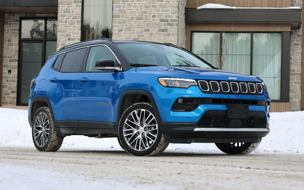 Blue Jeep Compass parked in snowy landscape in front of modern stone house winter wallpaper background