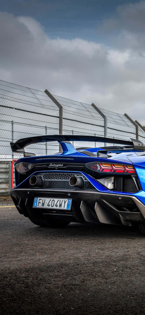 Blue Lamborghini parked by racetrack fence on open road luxury sports car wallpaper background