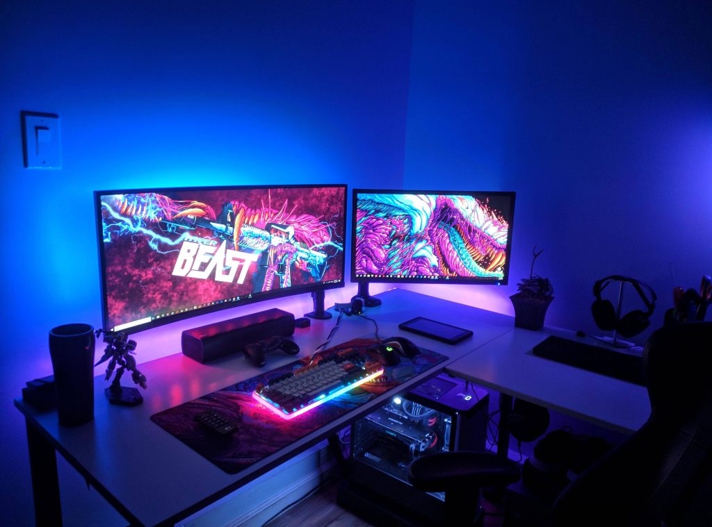 Blue-lit gaming desk with dual monitors showing Hyper Beast CS GO skin and RGB keyboard Wallpaper