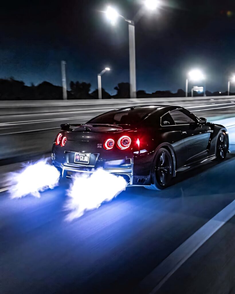 Blue Nissan R35 GTR racing at night with nitro flames from exhaust on highway wallpaper background