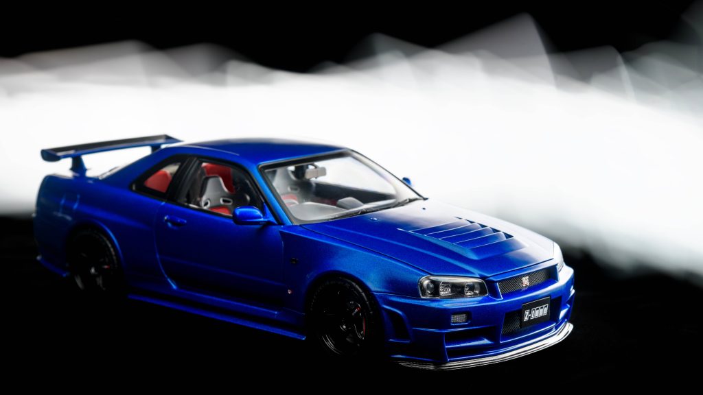 Macro photo of blue Nissan Skyline GT-R R34 scale model with dynamic white light trails background Wallpaper