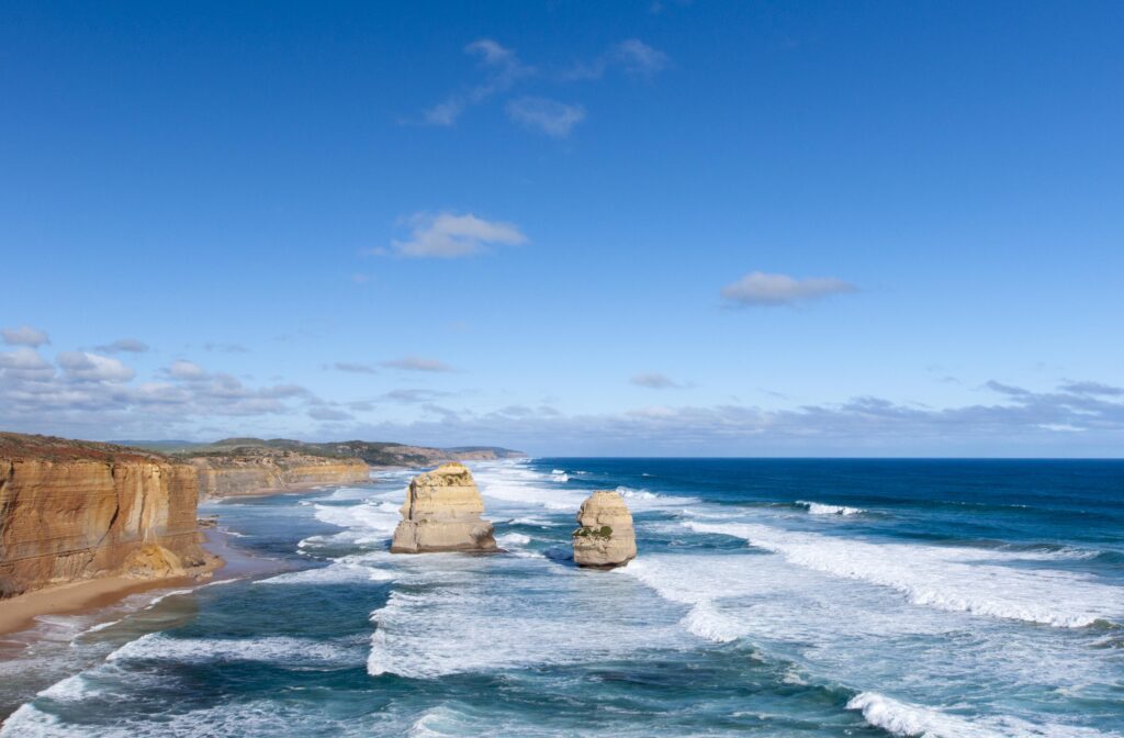 Blue ocean waves crashing on rugged coastline rocks under clear sky nature wallpaper background