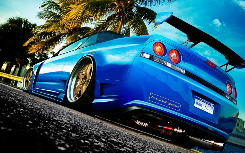 Blue R33 GTR with gold rims parked under palm trees against vivid sky automotive wallpaper background