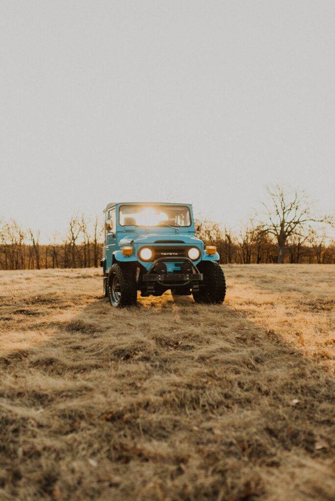 Blue SUV in Sunlit Field: Rustic Charm & Serene Landscape Wallpaper