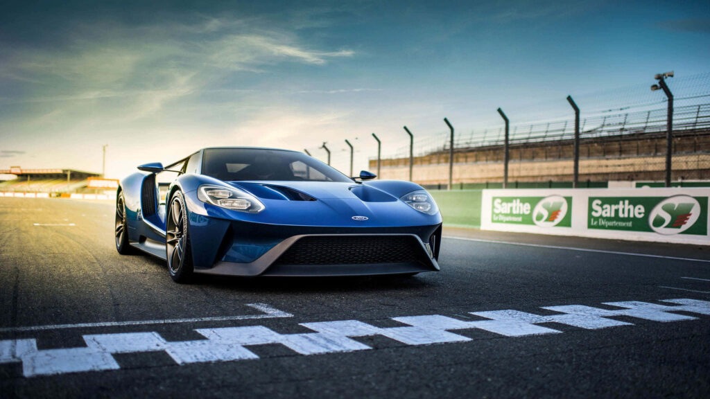 Blue sports car on race track with grandstands clear sky high performance speed background Wallpaper