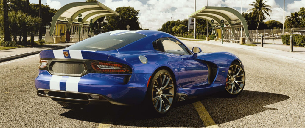 Blue sports car with white racing stripes parked on street with greenery and modern buildings Wallpaper