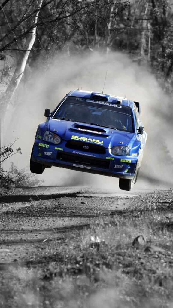 Blue Subaru rally car airborne on dusty off-road track high-speed racing wallpaper background