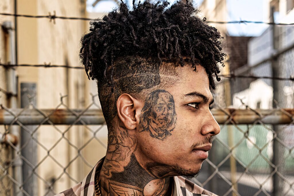 Close-up of Blueface with Benjamin Franklin tattoo on cheek urban chain-link fence background Wallpaper