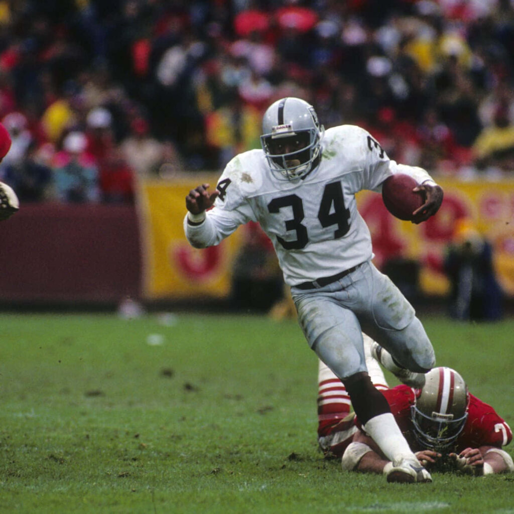 Bo Jackson sprinting down football field dodging tackle showcasing athleticism and determination Wallpaper