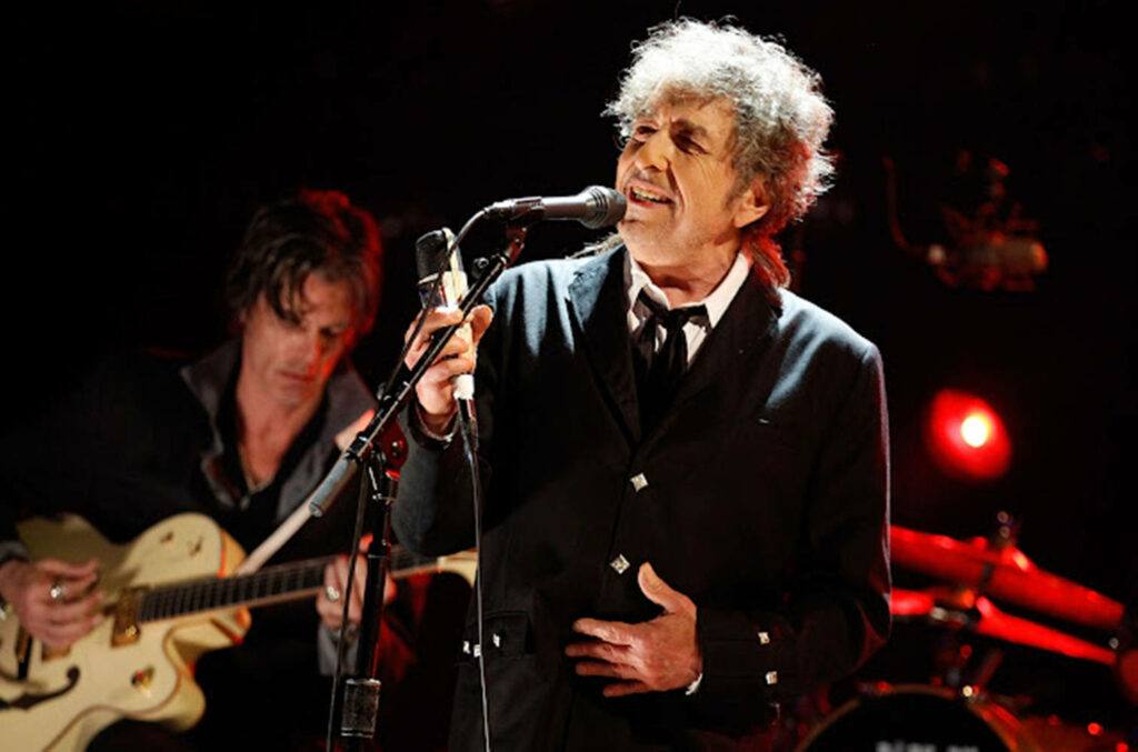 Bob Dylan passionately performing live on stage with band vibrant concert energy wallpaper background
