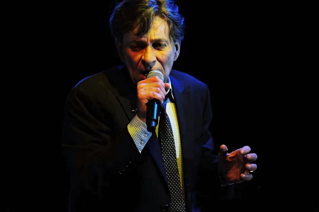 Bobby Caldwell singing passionately on stage in spotlight dark live music wallpaper background