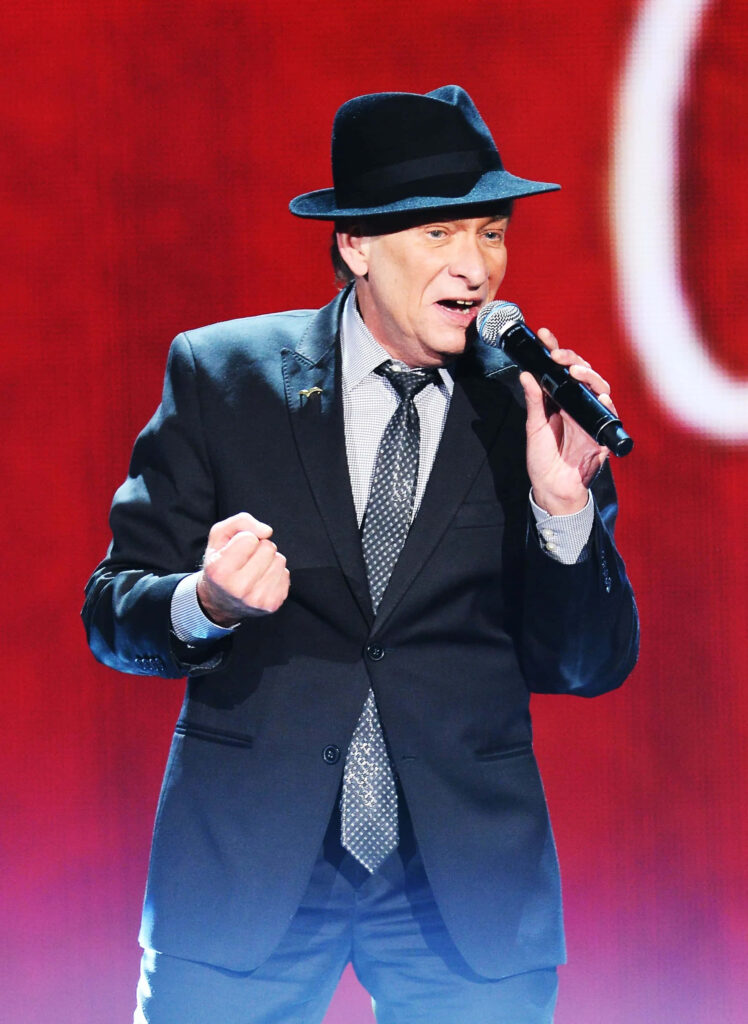 Bobby Caldwell live performance wearing black suit and hat vibrant red stage background wallpaper