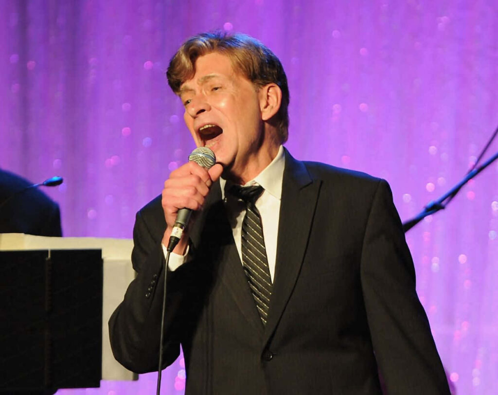 Bobby Caldwell live on stage in classic suit against purple backdrop performing passionately Wallpaper