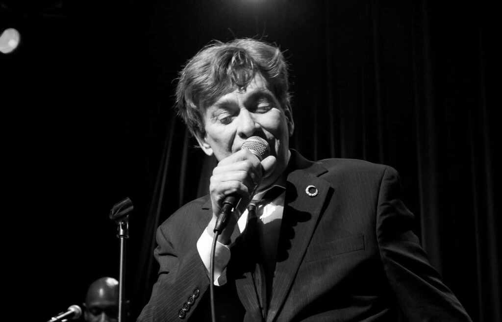 Bobby Caldwell live concert performance singing passionately in suit under bright stage lights Wallpaper