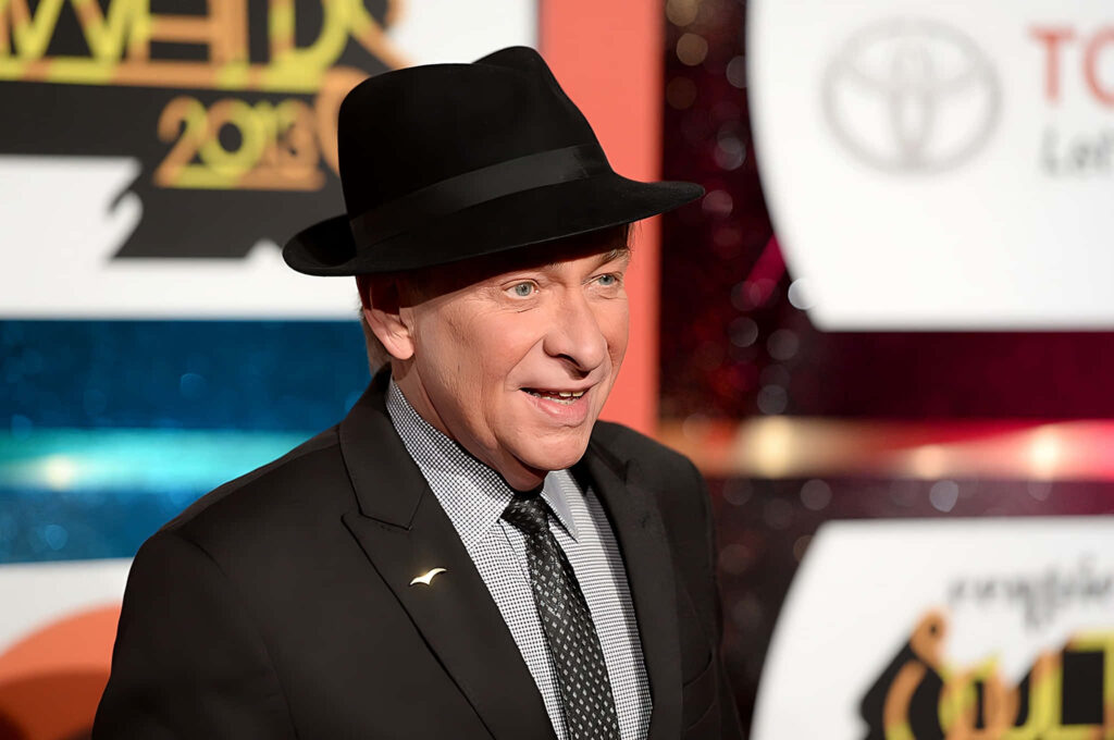 Bobby Caldwell smiling on stage wearing sharp suit and black hat under bright concert lights Wallpaper