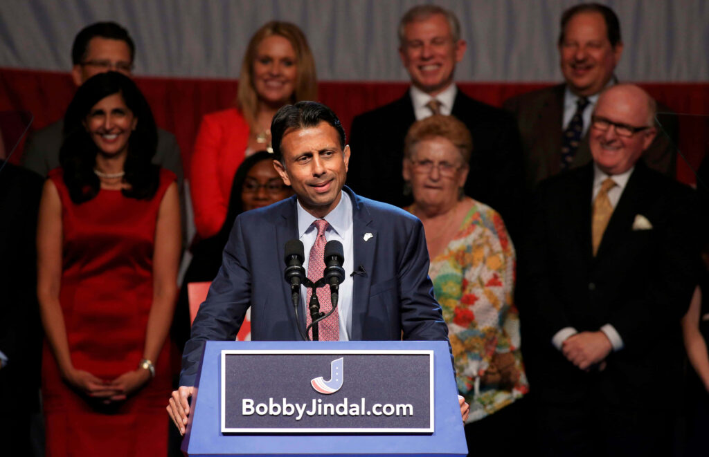Bobby Jindal speaking at campaign event with patriotic backdrop and supporters behind him Wallpaper