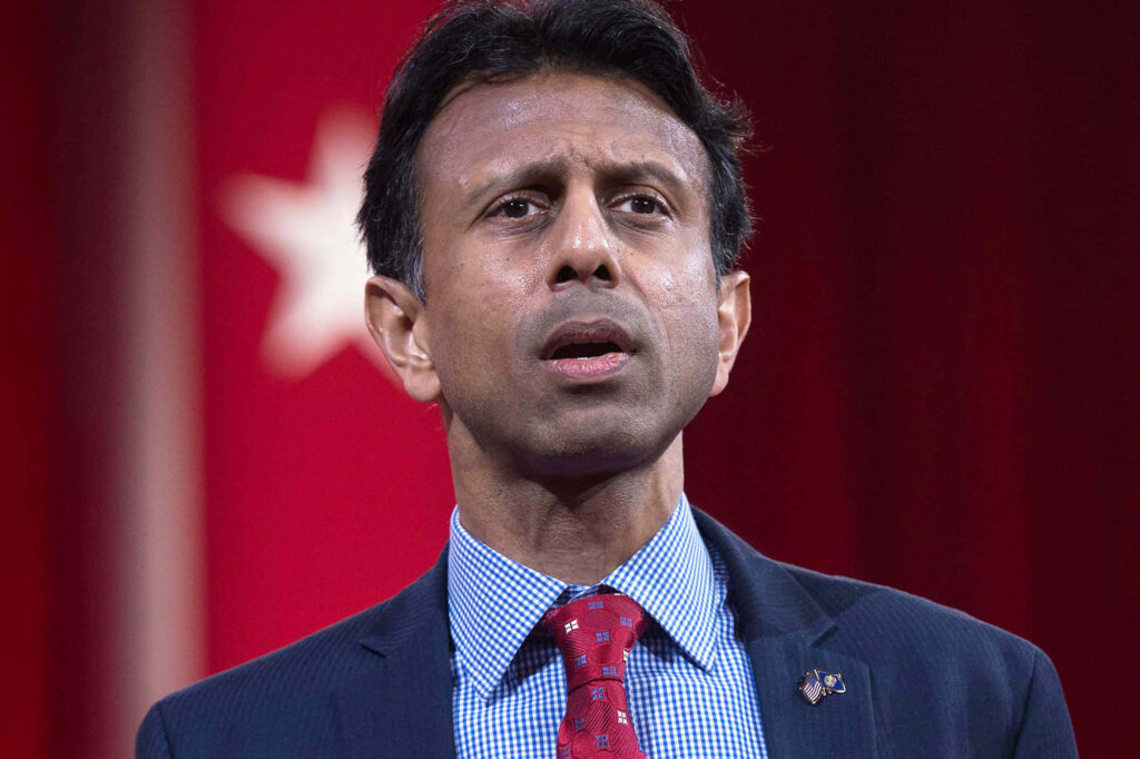 Bobby Jindal in formal suit with Governor pin against bold red background and white star wallpaper