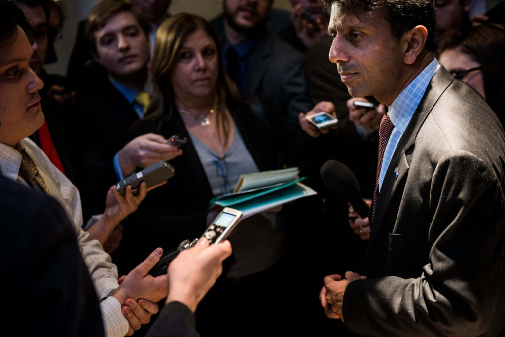 Bobby Jindal speaking to reporters at a press conference with microphones and recorders around him Wallpaper