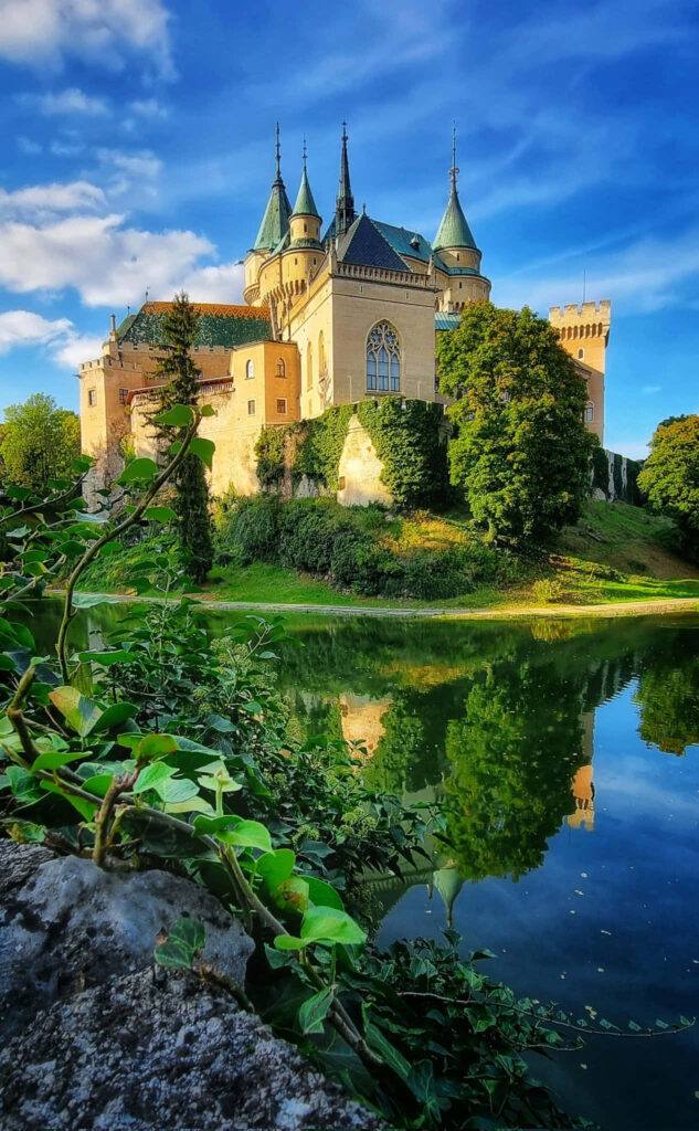 Bojnice Castle phone wallpaper vibrant medieval castle green trees blue sky reflection pond