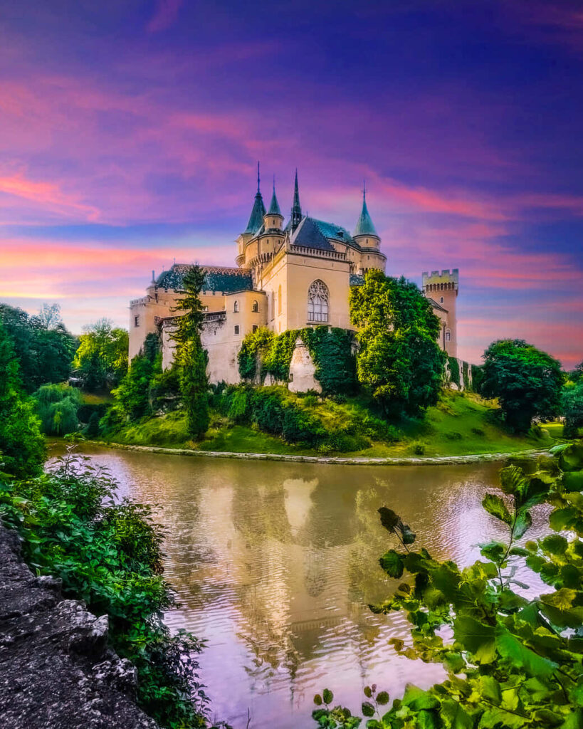 Bojnice Castle Slovakia purple sky sunset vibrant greenery and reflective moat fairytale wallpaper