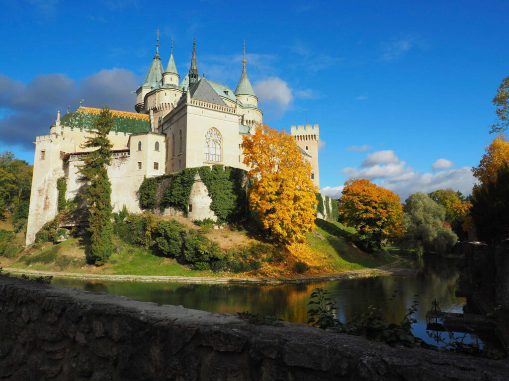 Bojnice Castle in Slovakia reflected in water with autumn foliage under a vivid blue sky Wallpaper