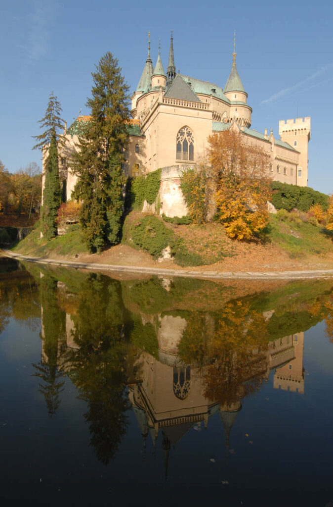 Bojnice Castle reflected in lake with autumn trees and clear blue sky wallpaper background