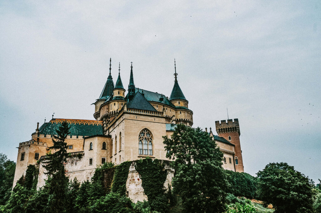 Bojnice Castle silhouette with turrets against moody gray sky and lush green trees landscape Wallpaper