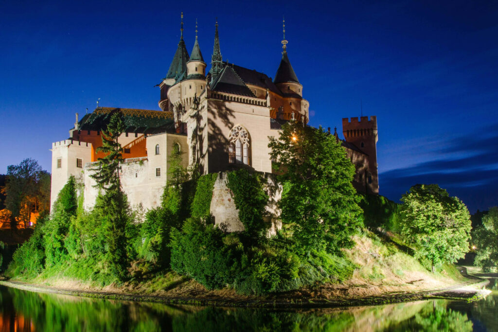Bojnice Castle Slovakia illuminated at night with water reflection and lush green surroundings wallpaper