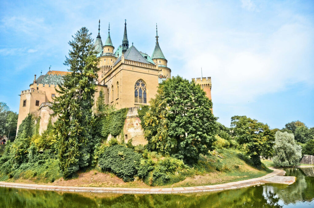 Bojnice Castle in Slovakia reflected in pond with lush greenery under clear vibrant blue sky wallpaper