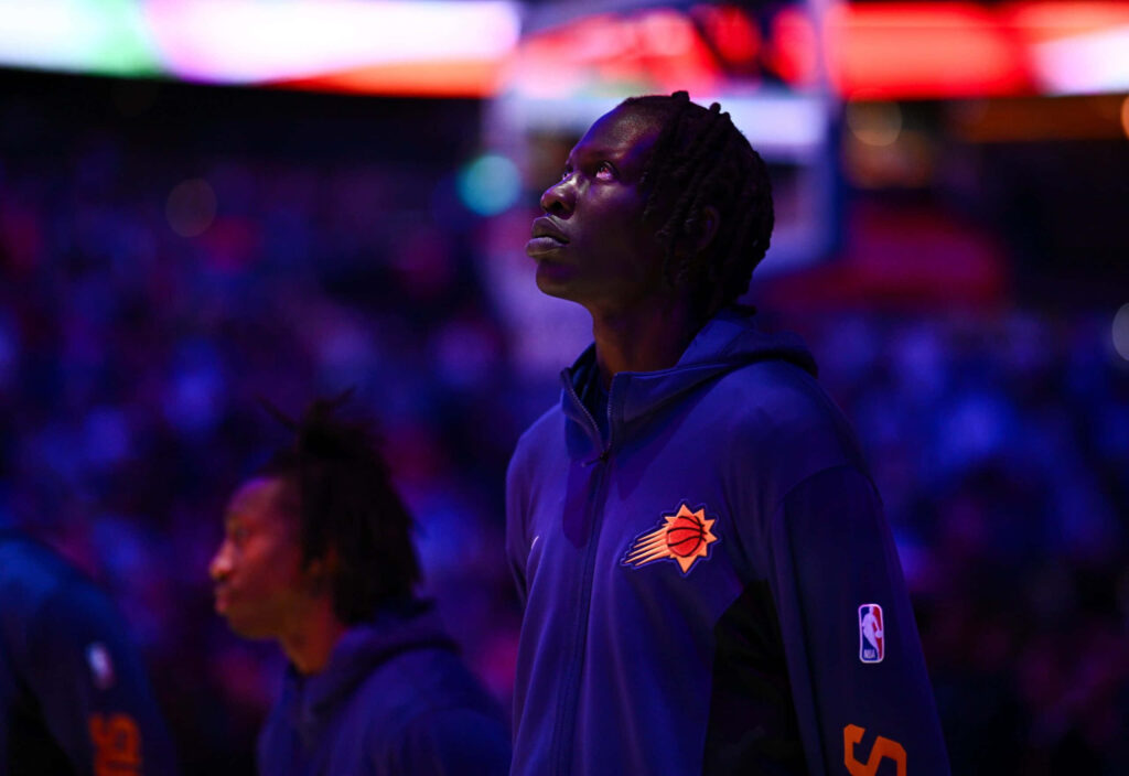 Bol Bol courtside in Phoenix Suns hoodie with vibrant arena lighting contemplative moment wallpaper