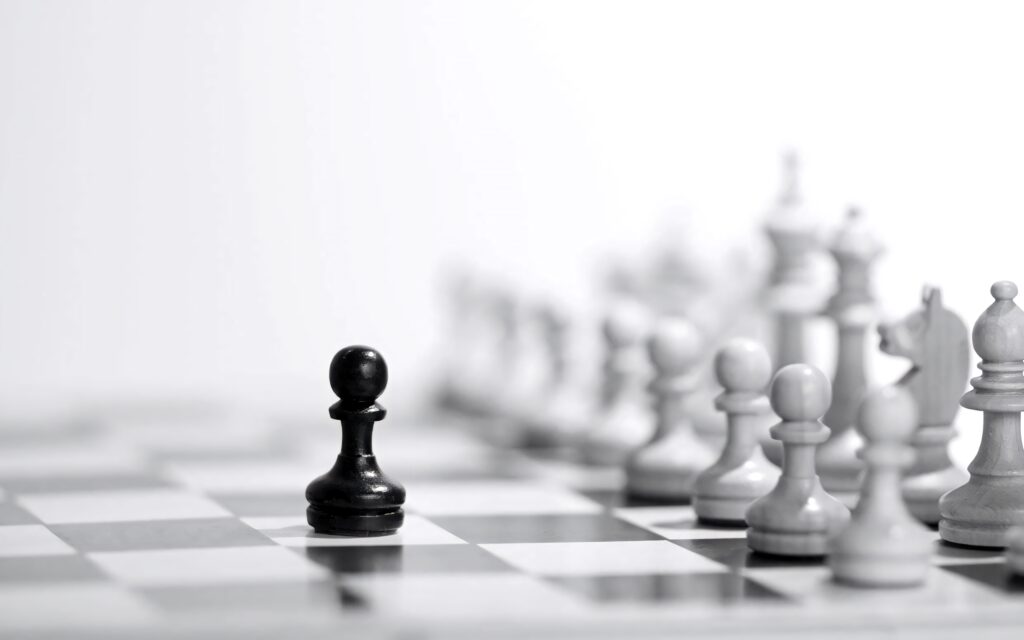 Black pawn stands alone on chessboard with blurred white pieces background minimalist strategy wallpaper