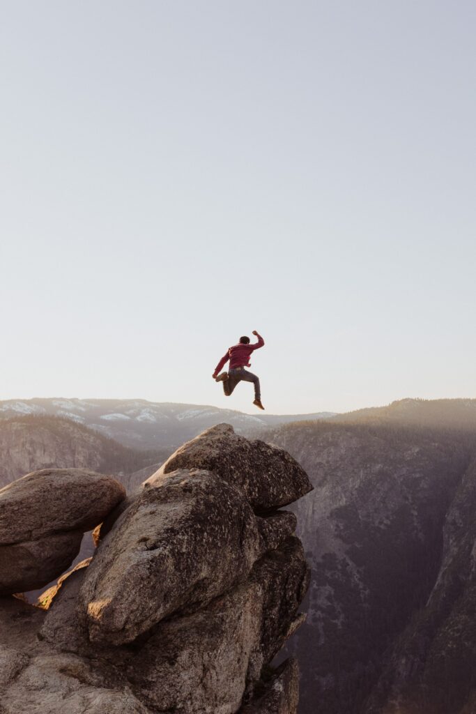 Man jumping between rugged mountain rocks at sunrise symbolizing freedom and adventure outdoors Wallpaper