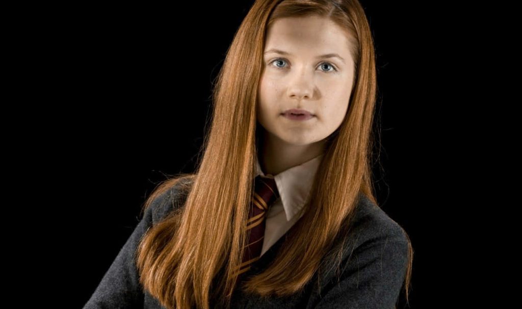 Bonnie Wright as Ginny Weasley in Gryffindor uniform with red hair on black background Wallpaper