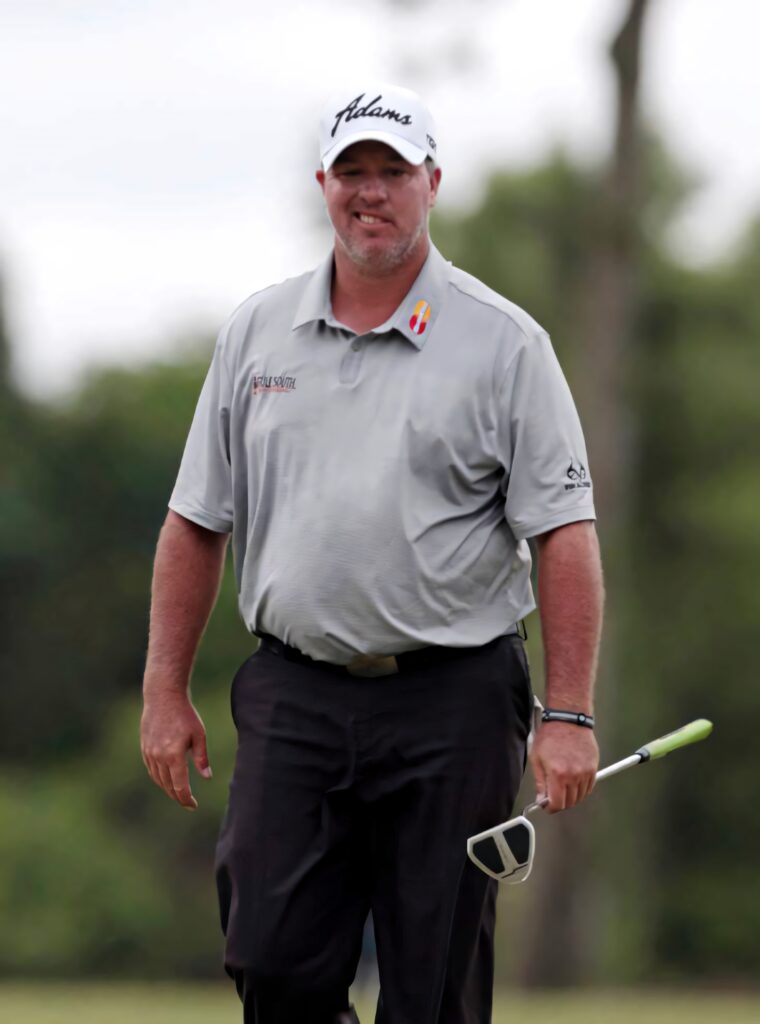 Boo Weekley walking on green golf course holding putter wearing gray shirt black pants white cap Wallpaper