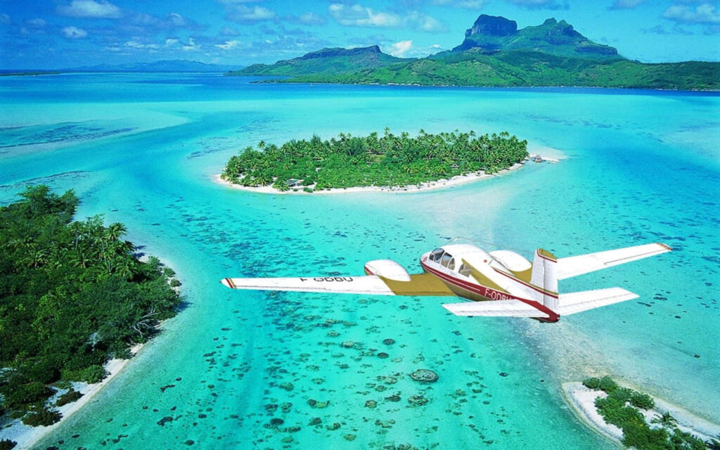 Small plane flying over turquoise waters and lush greenery of tropical Bora Bora island paradise Wallpaper