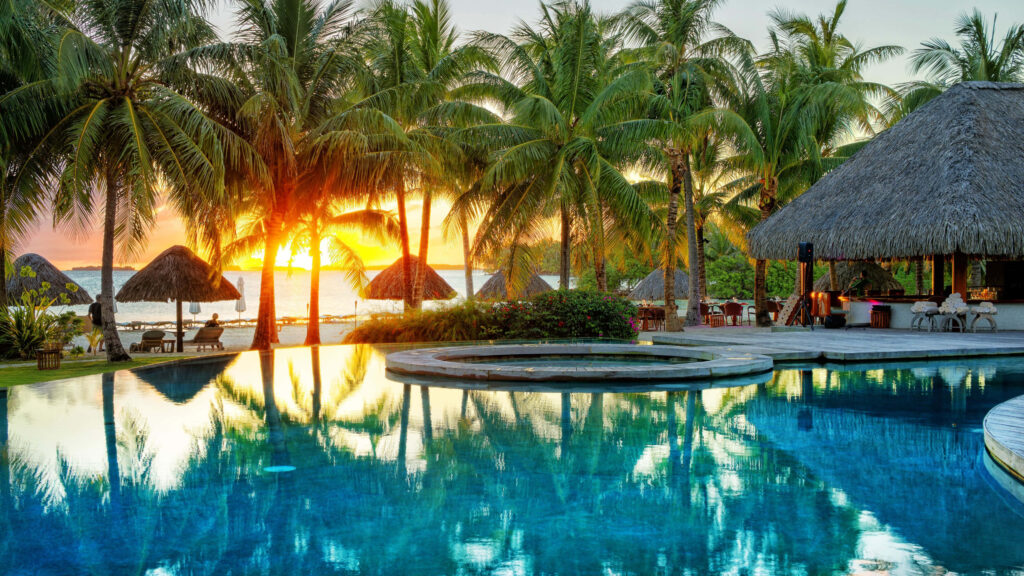 Luxurious Bora Bora pool at sunset with tall palm trees and thatched huts tropical wallpaper