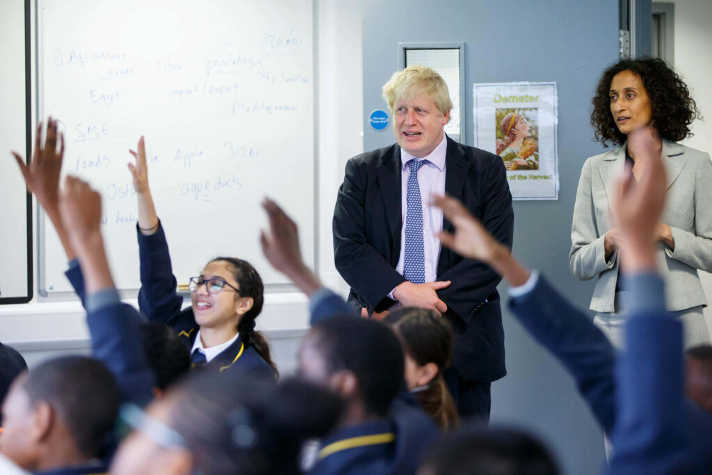 Boris Johnson in classroom with British teacher and eager students raised hands educational leadership Wallpaper
