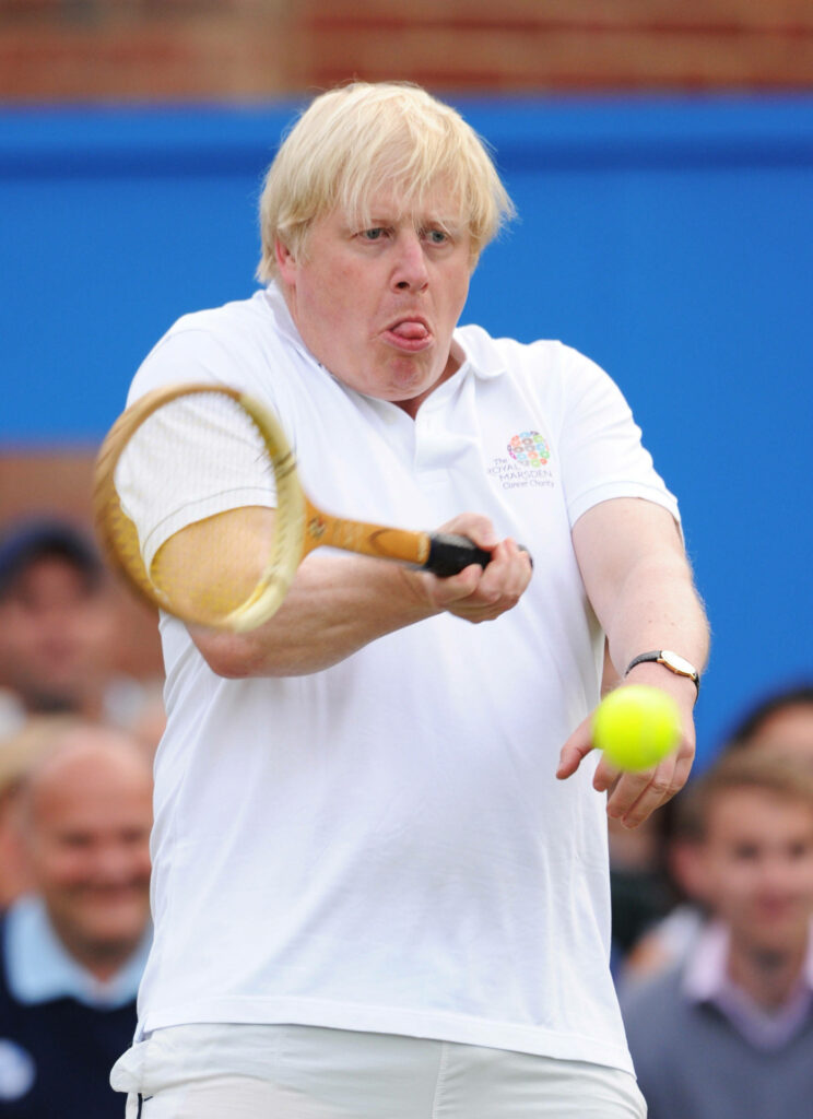 Boris Johnson playing tennis in white polo and shorts hitting ball with wooden racket wallpaper