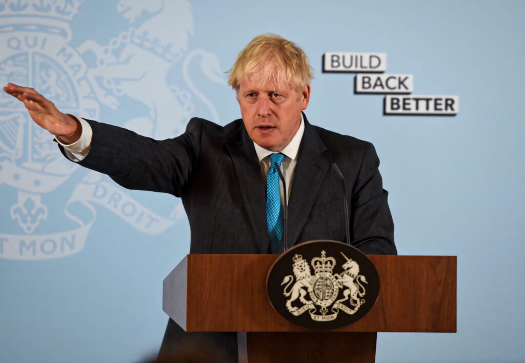 Boris Johnson raising arm at podium in dark suit with Build Back Better blue background wallpaper