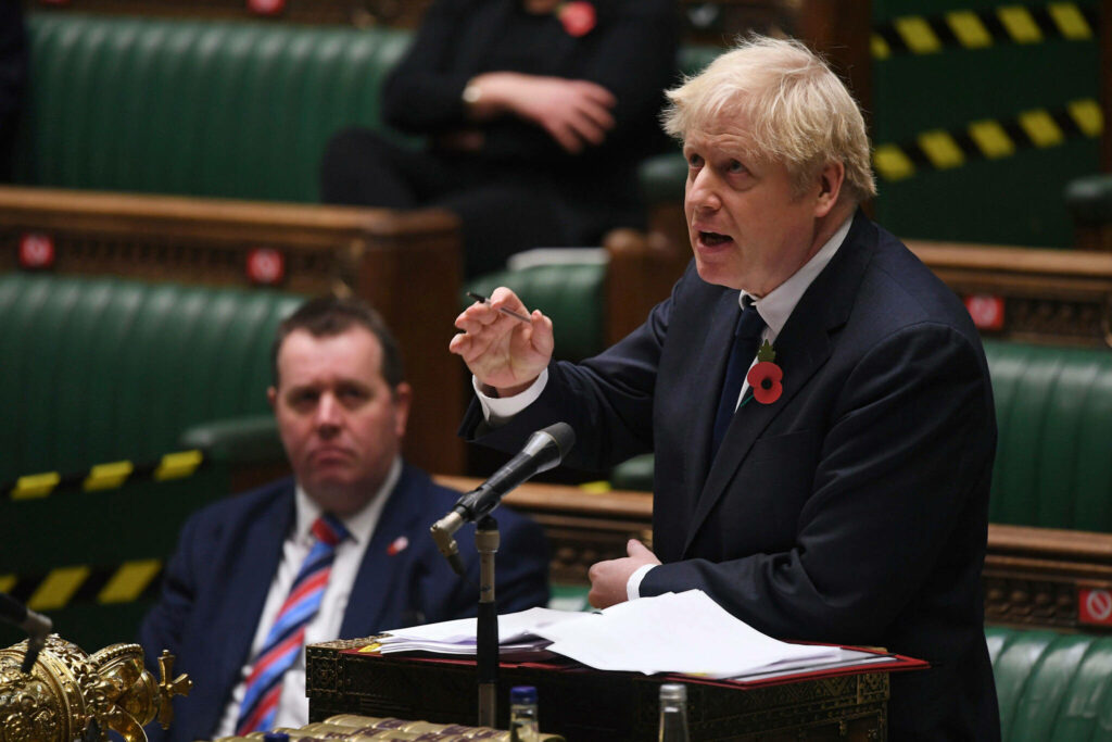 Boris Johnson delivering passionate speech in UK Parliament with green benches and documents Wallpaper