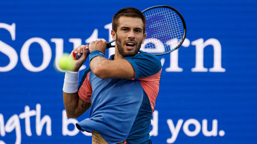 Borna Coric tennis action mid-swing vibrant blue background dynamic sportswear energy motion Wallpaper