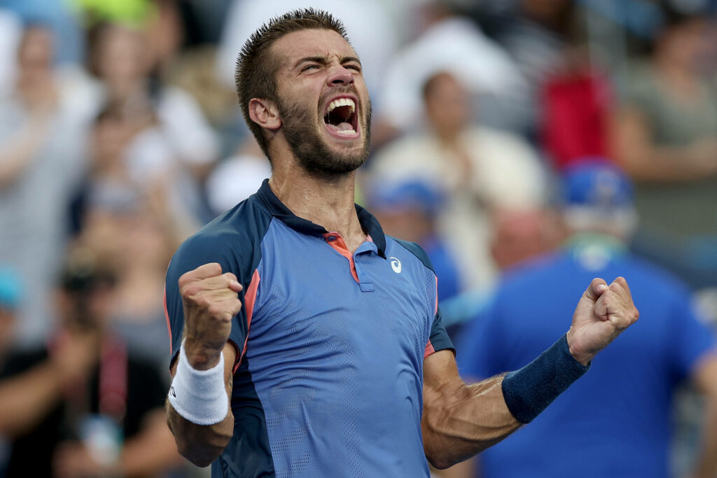 Borna Coric celebrating victory with clenched fists vibrant stadium blue tones intense tennis action Wallpaper