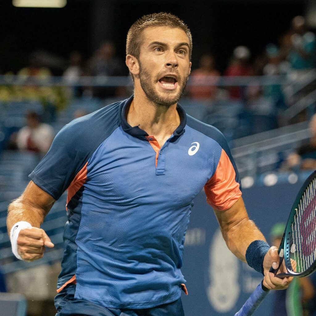 Borna Coric celebrating on court in blue and orange tennis gear high energy sports wallpaper background